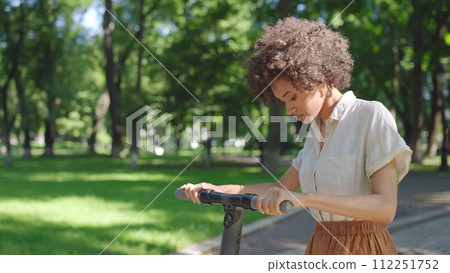 Young biracial woman learning to ride electric scooter in park, first experience Young biracial woman learning to ride electric scooter in park, first experience 112251752