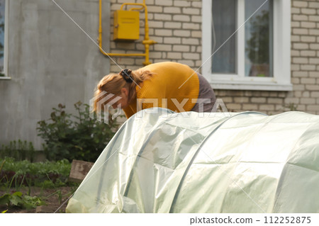 Woman farmer actively involved in setting up a low tunnel greenhouse for sustainable farming practices. Copy space. Blurred background 112252875