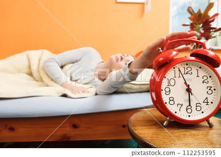 Woman waking up turning off alarm clock in morning Woman waking up turning off alarm clock in morning 112253595