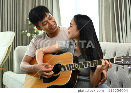 Affectionate Asian couple playing guitar while relaxing on weekend at home Affectionate Asian couple playing guitar while relaxing on weekend at home 112254094