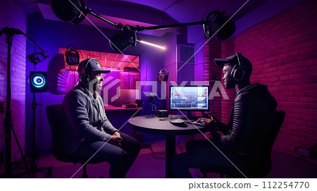 Two men wearing headphones are sitting in a room with purple lig 112254770