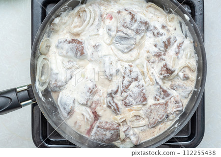 Pieces of beef liver stewed in sour cream with onions in a pan. 112255438
