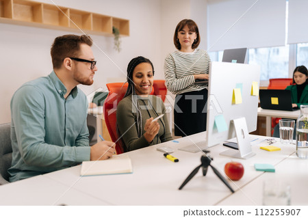 Cheerful multiethnic business team brainstorming using laptop computer at workplace. Focused multiracial coworkers group discuss corporate project during teamwork, working together at open space. 112255907