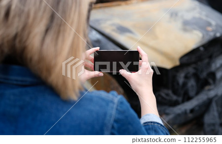 Insurance agent woman photographs burned-out car on smartphone Insurance agent woman photographs burned-out car on smartphone 112255965