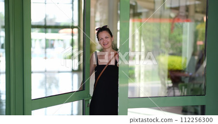Smiling young woman opening front door to hotel house and shop Smiling young woman opening front door to hotel house and shop 112256300