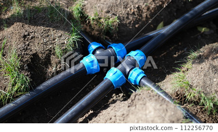 Black long pipe lies and tee adapter in dug-out earth closeup 112256770