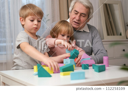 Grandfather playing toys with grandson and young granddaughter indoor. Old man grandpa studying with his grandchildren at weekend. Senior male having fun with kids. Happy multigeneration family video Grandfather playing toys with grandson and young granddaughter indoor. Old man grandpa studying with his grandchildren at weekend. Senior male having fun with kids. Happy multigeneration family video 112258109
