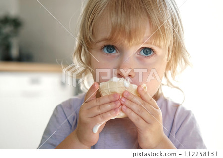 Baby girl enjoying ice cream. Pretty little toddler eating an ice-cream indoors, at home. Dining room background. Small child eats plombir and cream messy on her mouth. Cute kid with tasty sweet food. Baby girl enjoying ice cream. Pretty little toddler eating an ice-cream indoors, at home. Dining room background. Small child eats plombir and cream messy on her mouth. Cute kid with tasty sweet food. 112258131