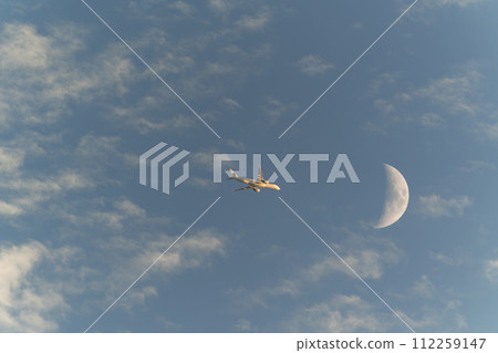一架客機飛過月亮進入夕陽 112259147