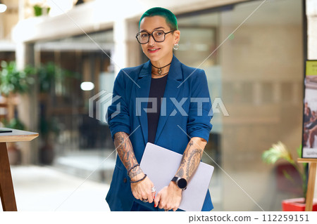 A woman with green hair and tattoos smiles while holding a laptop in formal wear A woman with green hair and tattoos smiles while holding a laptop in formal wear 112259151