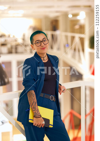 Woman in a blue blazer and glasses standing on a railing with a yellow folder Woman in a blue blazer and glasses standing on a railing with a yellow folder 112259155