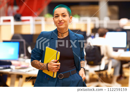 A woman with blue hair is smiling while holding a yellow book in an office 112259159