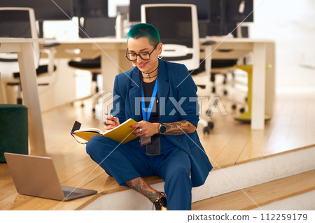 Creative smiling tattooed business woman with green short hair working on laptop in modern office Creative smiling tattooed business woman with green short hair working on laptop in modern office 112259179