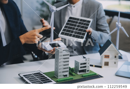 Two Young Engineers Expertise in Solar Cell Installation Meetings and Discussion in The Job. Planning to Install Solar Photovoltaic Panels on Roof Top in The Office Room with Factory Building Plan. Two Young Engineers Expertise in Solar Cell Installation Meetings and Discussion in The Job. Planning to Install Solar Photovoltaic Panels on Roof Top in The Office Room with Factory Building Plan. 112259549