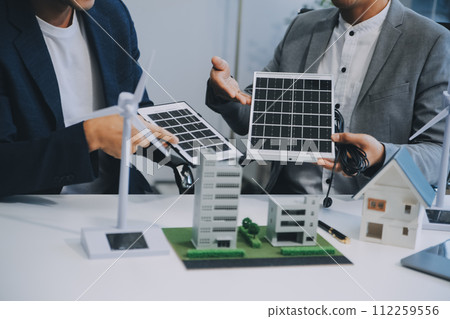 Two Young Engineers Expertise in Solar Cell Installation Meetings and Discussion in The Job. Planning to Install Solar Photovoltaic Panels on Roof Top in The Office Room with Factory Building Plan. 112259556