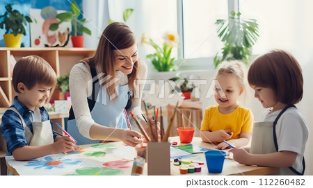 A female teacher is sitting at a table with three children. The A female teacher is sitting at a table with three children. The 112260482