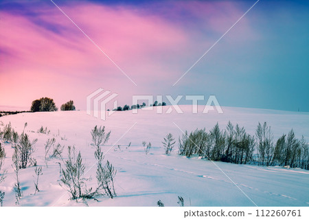 Hilly field covered with snow. Snowy winter rural landscape during sunset with colorful sky 112260761