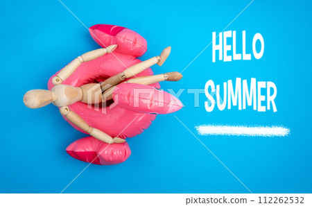 Wooden mannequin lounges on a whimsical inflatable flamingo raft, beneath a cheerful Hello Summer inscription on a bright blue background. Wooden mannequin lounges on a whimsical inflatable flamingo raft, beneath a cheerful Hello Summer inscription on a bright blue background. 112262532