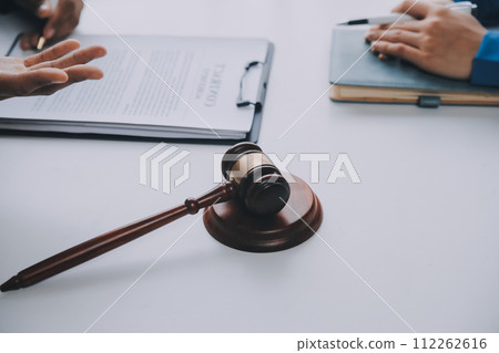 Justice and Law concept. Legal counsel presents to the client a signed contract with gavel and legal law or legal having team meeting at law firm in background 112262616