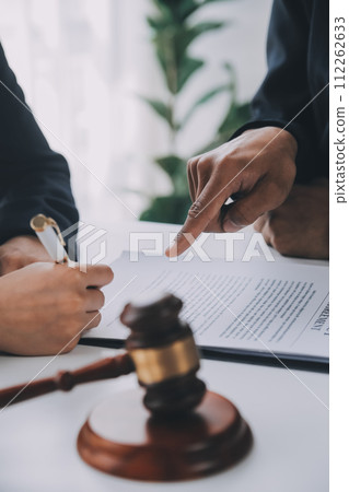 Justice and Law concept. Legal counsel presents to the client a signed contract with gavel and legal law or legal having team meeting at law firm in background Justice and Law concept. Legal counsel presents to the client a signed contract with gavel and legal law or legal having team meeting at law firm in background 112262633