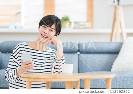 A young woman who operates a smartphone in the living room. A young woman who operates a smartphone in the living room. 112262862