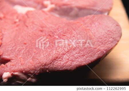 piece of raw meat lies on a cutting board on a dark background. Close-up of beef meat fibers 112262995