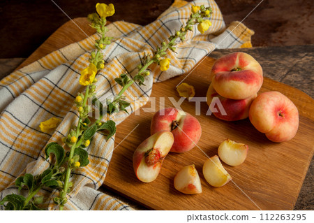 Cutting board with cut and whole saturn peaches or flat peaches on wooden background with yellow kitchen towel.. Cutting board with cut and whole saturn peaches or flat peaches on wooden background with yellow kitchen towel.. 112263295