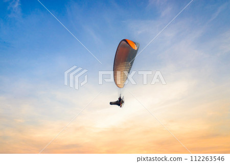 Motor Paraglider flying over the surface of the water in the evening Motor Paraglider flying over the surface of the water in the evening 112263546