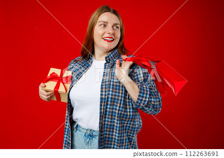 Portrait of cheerful, happy woman smiling excited. Girl holding wrapped present and paper bags, celebrating birthday or sales on red background. Valentine's Day Women's Day birthday holiday concept. Portrait of cheerful, happy woman smiling excited. Girl holding wrapped present and paper bags, celebrating birthday or sales on red background. Valentine's Day Women's Day birthday holiday concept. 112263691