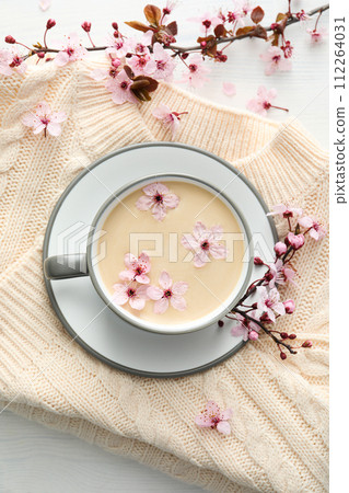 Spring twigs with flowers with a cup of hot drink, on a light wooden background. 112264031
