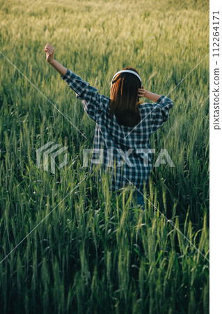 Young pretty woman in red summer dress and straw hat walking on yellow farm field with ripe golden wheat enjoying warm evening. Young pretty woman in red summer dress and straw hat walking on yellow farm field with ripe golden wheat enjoying warm evening. 112264171