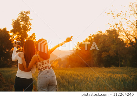 Young pretty woman in red summer dress and straw hat walking on yellow farm field with ripe golden wheat enjoying warm evening. Young pretty woman in red summer dress and straw hat walking on yellow farm field with ripe golden wheat enjoying warm evening. 112264240