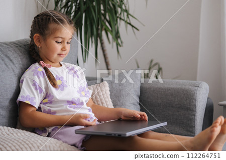 Smart little girl open gray laptop while she sitting on sofa at home 112264751