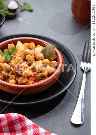 Homemade Ropa vieja, typical Canarian dish of chickpeas stew with chicken and potatoes in a earthenware casserole on marble table. Vertical format. Homemade Ropa vieja, typical Canarian dish of chickpeas stew with chicken and potatoes in a earthenware casserole on marble table. Vertical format. 112265398