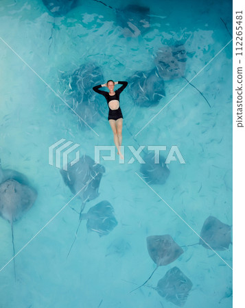 Woman swimming with stingrays in Maldives. Sting ray fishes and woman swimming in blue sea, Aerial view 112265481
