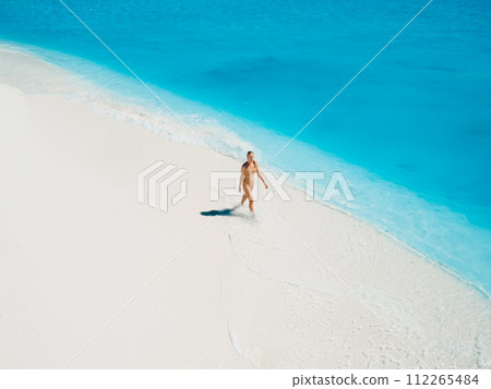 Woman in swimsuit walking on tropical white sandy beach with turquoise ocean water. Aerial view Woman in swimsuit walking on tropical white sandy beach with turquoise ocean water. Aerial view 112265484