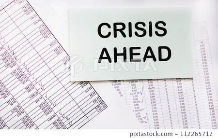 Notepad with the text A crisis is ahead against the backdrop of financial calculations. Notepad with the text A crisis is ahead against the backdrop of financial calculations. 112265712