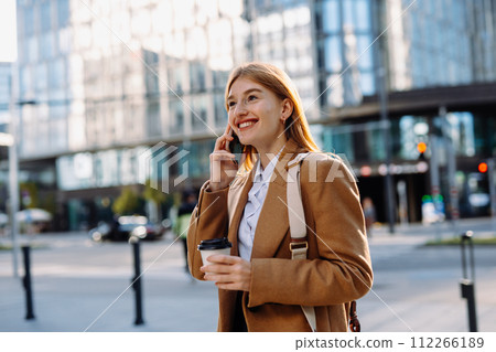 Young lady in white shirt with takeaway cup of coffee answering phone call 112266189