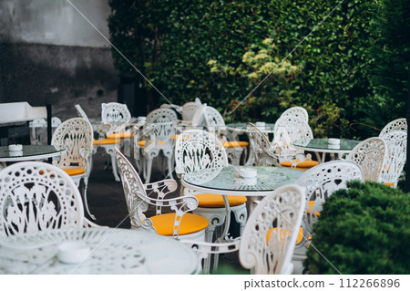 Empty restaurant summer terrace with white tables and chairs. Restaurant tables waiting for customers at an outdoor terrace. Cozy street with tables of cafe Empty restaurant summer terrace with white tables and chairs. Restaurant tables waiting for customers at an outdoor terrace. Cozy street with tables of cafe 112266896