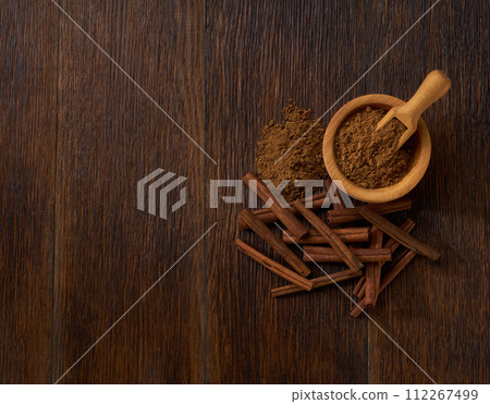 cinnamon powder in a wooden bowl on a dark wooden table , top view. cinnamon powder in a wooden bowl on a dark wooden table , top view. 112267499