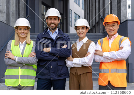 A diverse group of construction professionals with hard hats standing confidently outside a building. 112268600