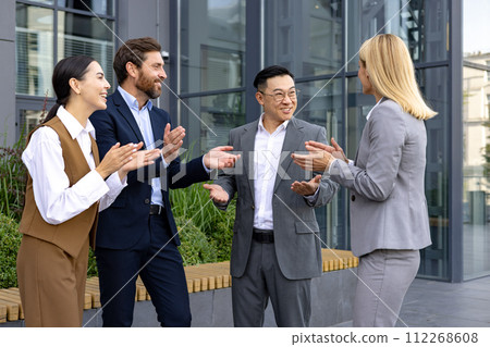 Group of happy business professionals clapping hands in celebration of a successful meeting outdoors near modern office. Group of happy business professionals clapping hands in celebration of a successful meeting outdoors near modern office. 112268608