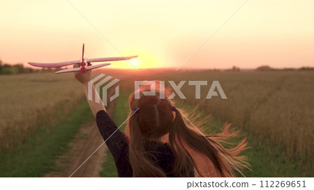 girl plays countryside toy airplane, girl hair flutters wind while running airplane sunset, child holds airplane hand sunset, dreams flying, kid child girl daughter runs with toy airplane hand park. 112269651