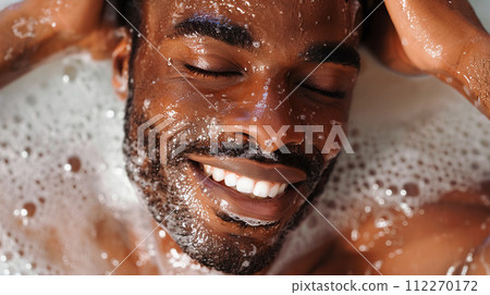 AI-generated content. A dark-skinned man with his eyes closed and a joyful expression on his face enjoys bubble bath, drops of water glistening on his face, emphasizing the moment of pure bliss. Soft 112270172