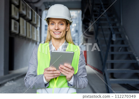 Professional caucasian woman in helmet and neon yellow vest standing at construction with digital tablet in hands. Experienced female architect checking house building process and entering data. Professional caucasian woman in helmet and neon yellow vest standing at construction with digital tablet in hands. Experienced female architect checking house building process and entering data. 112270349