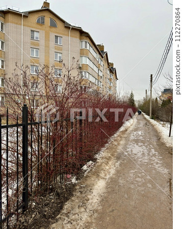 Melting dirty snow on the streets of the city during the daytime in winter. The pedestrian road along the fence has snow with sand and mud. Traces of people and pets Melting dirty snow on the streets of the city during the daytime in winter. The pedestrian road along the fence has snow with sand and mud. Traces of people and pets 112270864