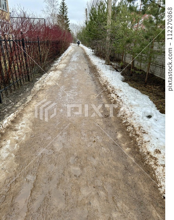 Melting dirty snow on the streets of the city during the daytime in winter. The pedestrian road along the fence has snow with sand and mud. Traces of people and pets Melting dirty snow on the streets of the city during the daytime in winter. The pedestrian road along the fence has snow with sand and mud. Traces of people and pets 112270868