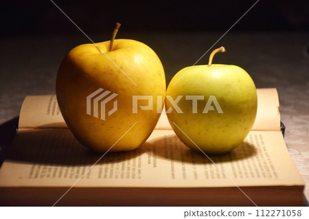 A stack of books in red covers and a red apple against the morning window. A metaphorical image of a good start to the 112271058
