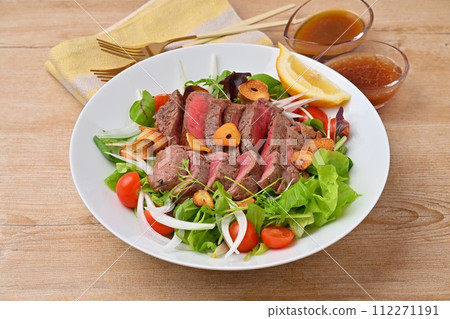 豐盛的牛排沙拉、蔬菜沙拉、牛大腿牛排和調味料。 豐盛的牛排沙拉、蔬菜沙拉、牛大腿牛排和調味料。 112271191