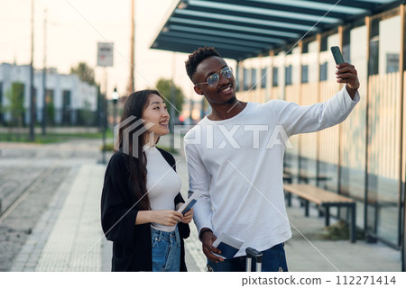 Cheerful multiracial male and female friends making selfie on smartphone with passports and tickets before joint trip. 112271414